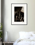 A framed wall art black-and-white photograph hangs on a light-colored wall above a white bed. A green potted plant and a white vase rest on the bedside table, adding mindful home decor touches.