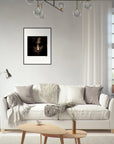 A modern living room with a white sofa, gray and beige pillows, and a cozy blanket, featuring framed wall art in a gallery-quality frame above the couch. There is a floor lamp, basket, coffee table, and window with white curtains.