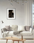 A modern living room with a white sofa, gray and beige pillows, a floor lamp, a small wooden coffee table, a basket with blankets, framed wall art, and a window with sheer curtains letting in natural light.