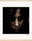 A grainy, high-contrast black and white close-up portrait of a person's face, partially obscured by dark hair. The intense expression and light wood border make it striking framed wall art for conscious interior design.