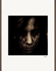 A dark, grainy close-up portrait of a person's face with long hair partially covering their features. The moody, intense image is presented in a gallery-quality frame with a white border, bringing mindful home decor to your space.