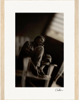 A sepia-toned fine art print of a person sitting barefoot on a chair, one knee drawn up, gazing thoughtfully into the distance. Perfect as inspirational wall art, it’s framed with a light wooden border for conscious interior design.