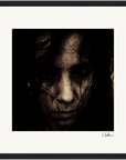 A dark, grainy close-up of a person's face with long hair partially covering their features, set against a plain background and framed in black. This fine art print adds a sophisticated, contemplative touch to mindful home decor.