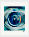 A close-up photo of the front door of an Electrolux washing machine with blue and green reflections on the glass. This fine art print features a digital, abstract effect, making it perfect for mindful home decor; a signature appears in the bottom right corner.
