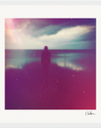 A person stands alone on a beach under a cloudy sky, facing the water. This inspirational wall art features a soft, dreamy effect with purple and pink light leaks, enhanced by a white border and signature in the bottom right corner.