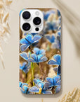 A smartphone with a case featuring an art print of blue butterflies on a natural background rests on a beige surface near dried grasses. The word “INTENTION” and a small symbol are printed at the bottom, adding artistic textures to the design.