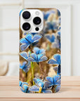 A smartphone case with a photo art design featuring multiple blue butterflies on grass, displayed upright on a wooden surface with a light-colored, blurred background. Textures and the word INTENTION appear near the bottom of the case.