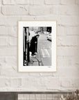 A gallery-quality frame showcases this black-and-white photograph, depicting an elderly person with a cane at a city street corner. The striking image adds inspirational wall art to any conscious interior design.