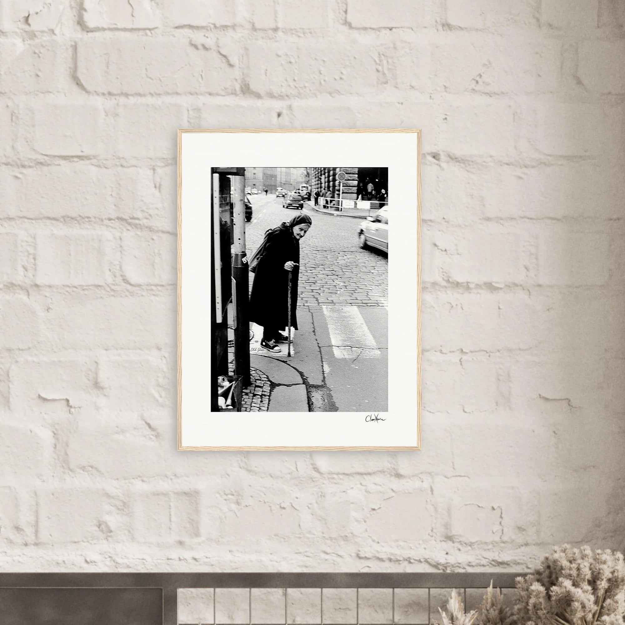 A gallery-quality frame showcases this black-and-white photograph, depicting an elderly person with a cane at a city street corner. The striking image adds inspirational wall art to any conscious interior design.