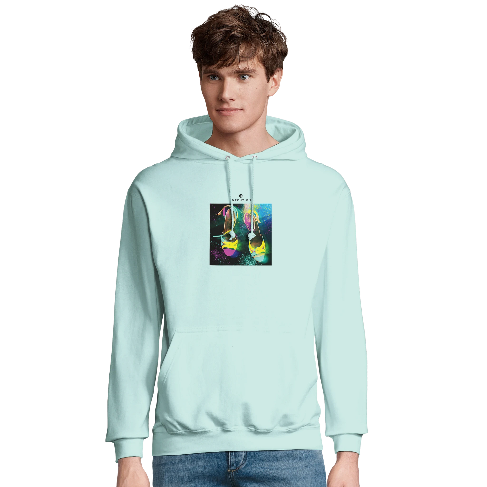 A young man wears a light blue hoodie from a mindful apparel collection, featuring a colorful graphic of two hanging sneakers against a multicolored background. He stands facing forward with a neutral expression.