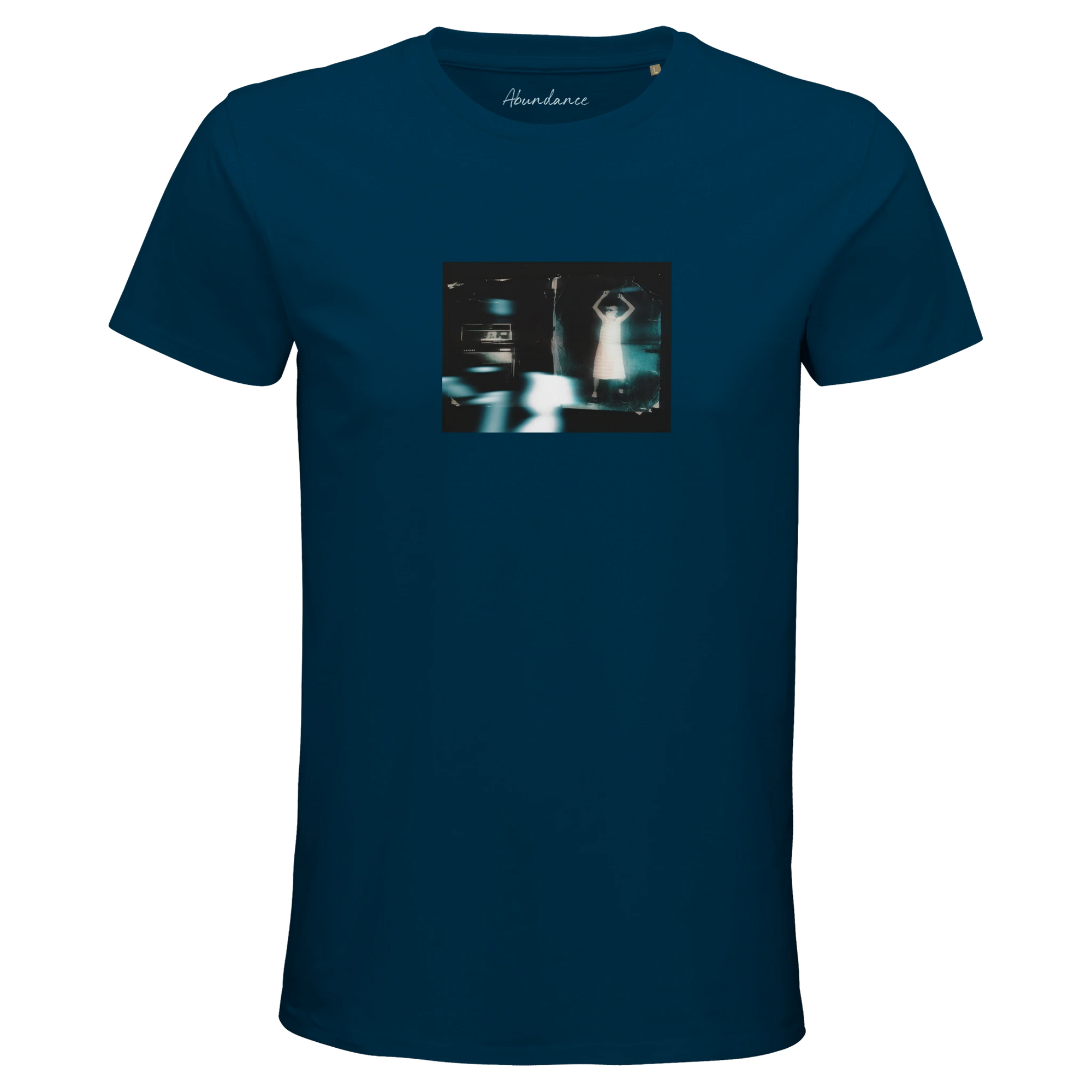 A denim t-shirt with an art print on the chest shows a blurred, blue-toned figure with raised arms by a car at night. "Abundance" is printed inside the collar, reflecting mindful apparel and conscious fashion.