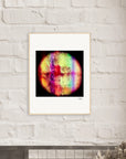 A framed inspirational wall art print featuring a colorful, circular pattern with red, green, yellow, and purple hues hangs on a white brick wall above a shelf, perfect for mindful home decor.