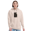A person with short brown hair wears a light beige hoodie featuring an art print graphic on the chest, paired with light blue jeans. The look reflects conscious fashion against a plain white background.