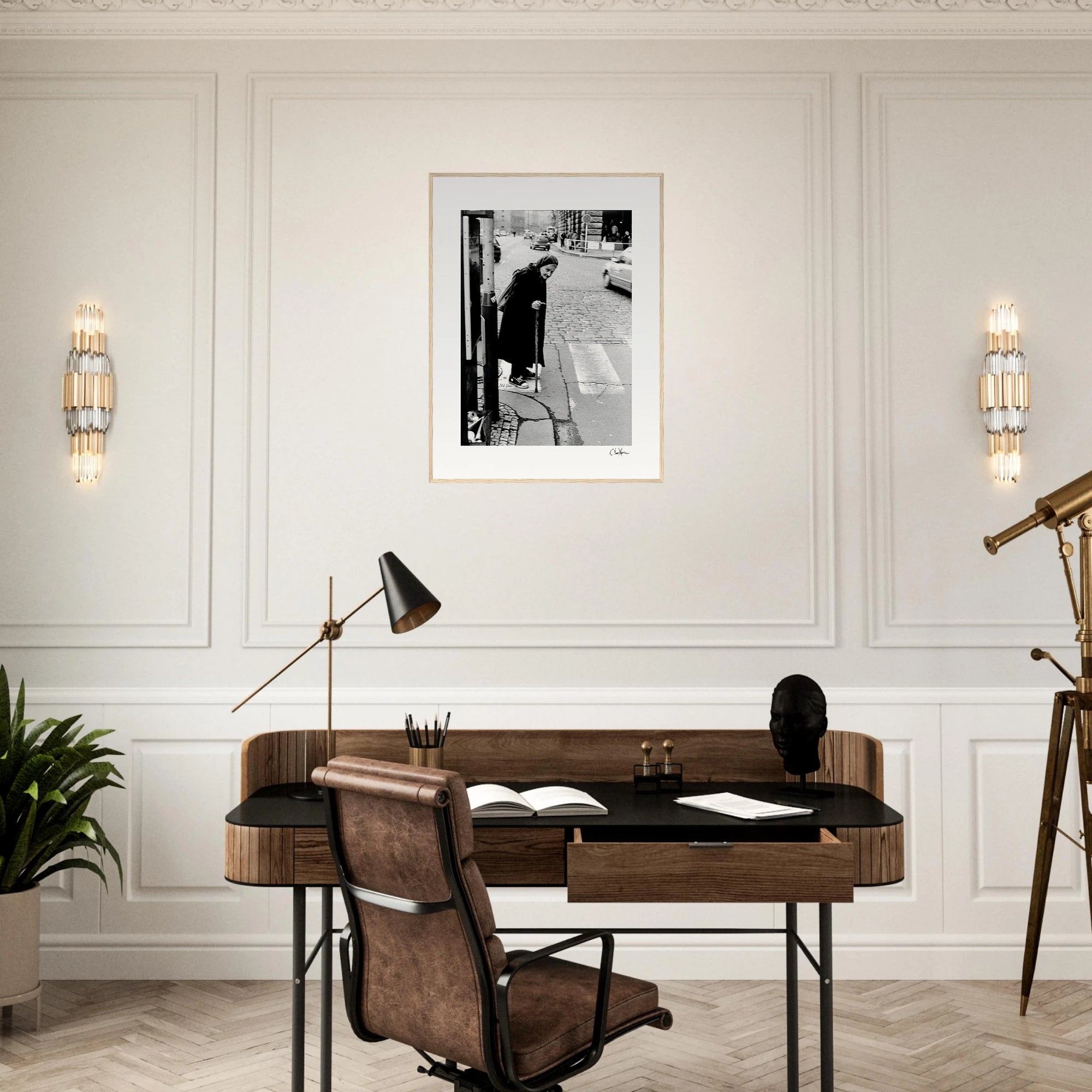 A modern home office features a wooden desk with a lamp, books, a chair, a telescope, and conscious interior design touches. Gallery-quality framed wall art hangs on the white paneled wall above the desk.