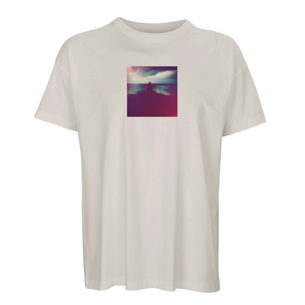 Off white short-sleeve t-shirt with a small, square, colorful art print on the chest showing a silhouetted figure by water under a cloudy purple and pink sky. Embrace conscious fashion with this unique design.