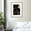 A framed wall art black-and-white photograph hangs on a light-colored wall above a white bed. A green potted plant and a white vase rest on the bedside table, adding mindful home decor touches.