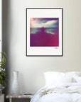 A framed fine art print hangs on a beige wall above a white bed. The image features a silhouette of a person and a colorful, blurry landscape. A potted plant and white vase sit on the bedside table, perfect for conscious interior design.