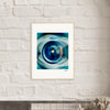 A framed fine art print featuring a close-up image of a washing machine door hangs on a white brick wall above a dark shelf with dried flowers in the foreground, adding an inspirational touch to conscious interior design.