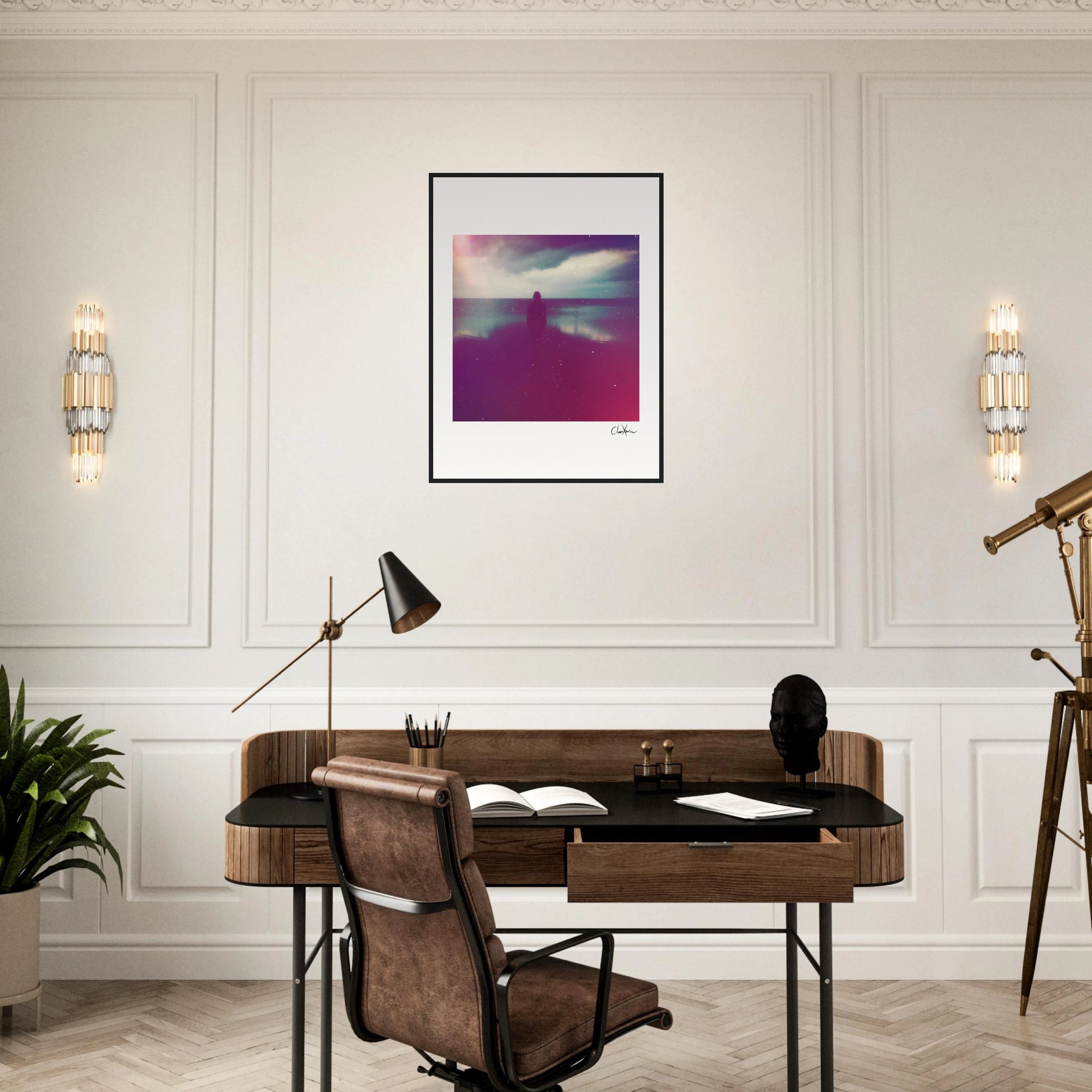 A modern home office with a wooden desk, brown chair, and decorative items including a plant, telescope, and black sculpture. A gallery-quality frame displays an abstract photograph centered on the white paneled wall above the desk.