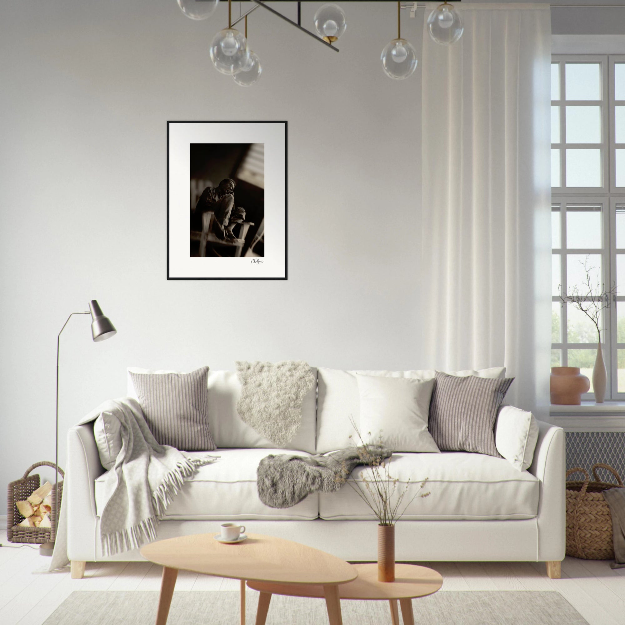 A modern living room with a white sofa, gray and beige pillows, a floor lamp, a small wooden coffee table, a basket with blankets, framed wall art, and a window with sheer curtains letting in natural light.