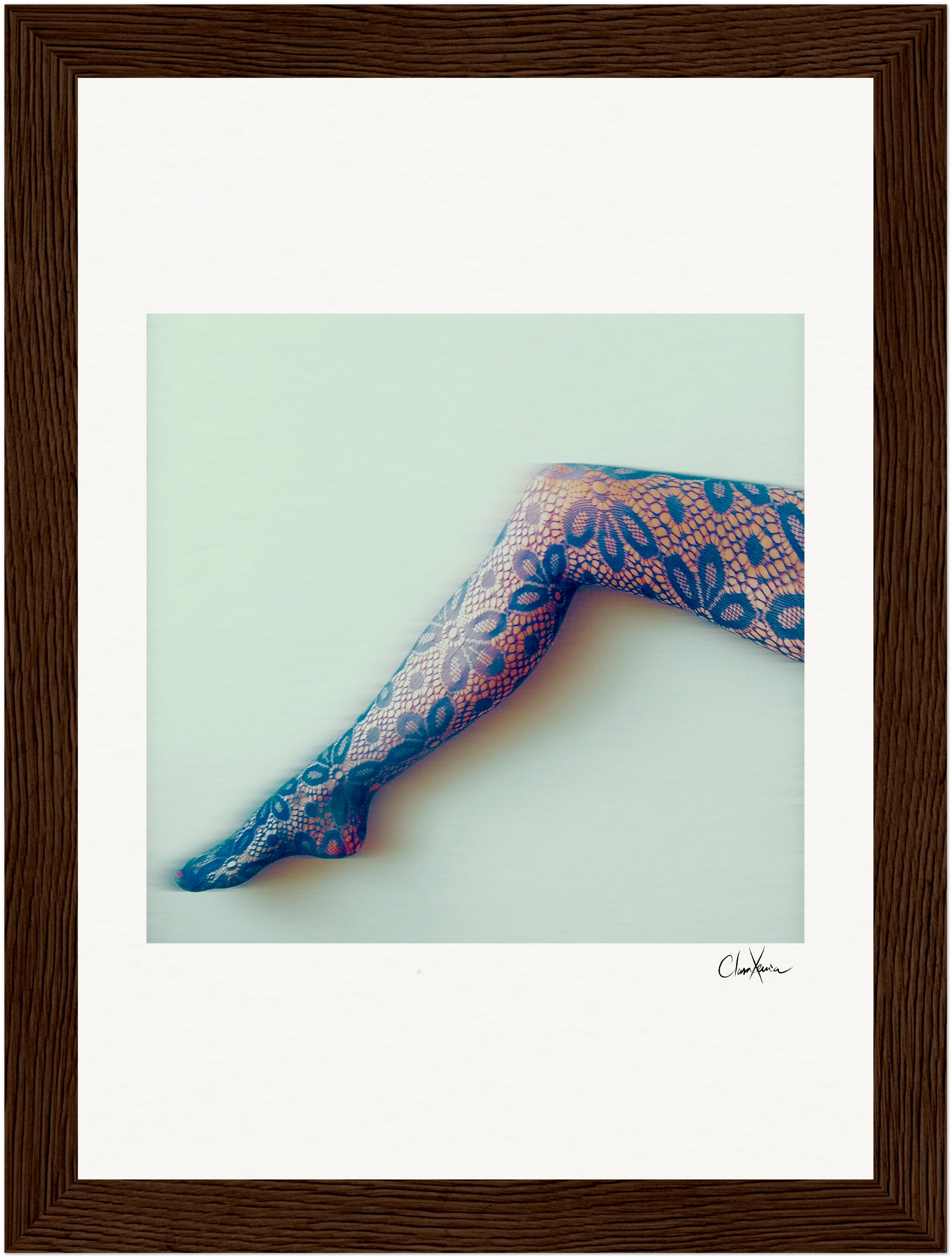 A framed photograph of a single outstretched leg in blue and pink patterned lace tights against a pale background, angled diagonally. This unique piece of inspirational wall art features a signature on the lower right corner of the white mat.