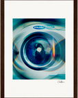 A close-up view of a washing machine door with abstract blue and green light reflections. This fine art print has a soft, blurred effect and is elegantly framed by a dark wooden border, making it stunning inspirational wall art.
