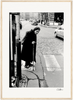 An elderly woman wearing a headscarf and dark clothing uses a cane to cross a cobblestone street. Cars are in the background, and pedestrians walk on the sidewalk. This black-and-white scene adds mindful home decor appeal to your space.