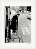 An elderly woman in a dark coat and headscarf leans on a cane while stepping onto a cobblestone street at a crosswalk, with cars and pedestrians in the background—an evocative scene perfect as inspirational wall art or a fine art print.