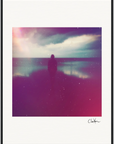 A silhouette of a person stands by a calm body of water under a cloudy sky, with a colorful, hazy filter. Presented as inspirational wall art in a gallery-quality frame, the photograph is signed in the bottom right corner.