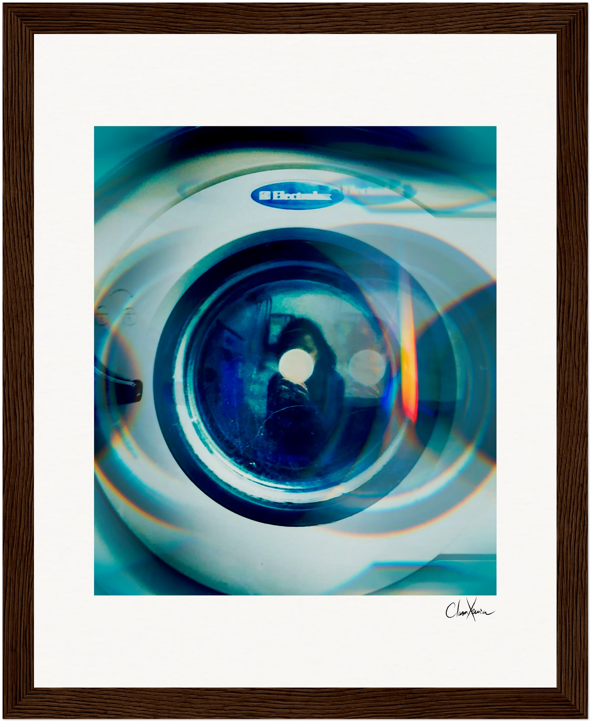 A gallery-quality framed photograph of a front-loading Electrolux washing machine door, shot close-up with a blue tint and light reflections, signed by the artist in the bottom right corner—perfect as inspirational wall art.
