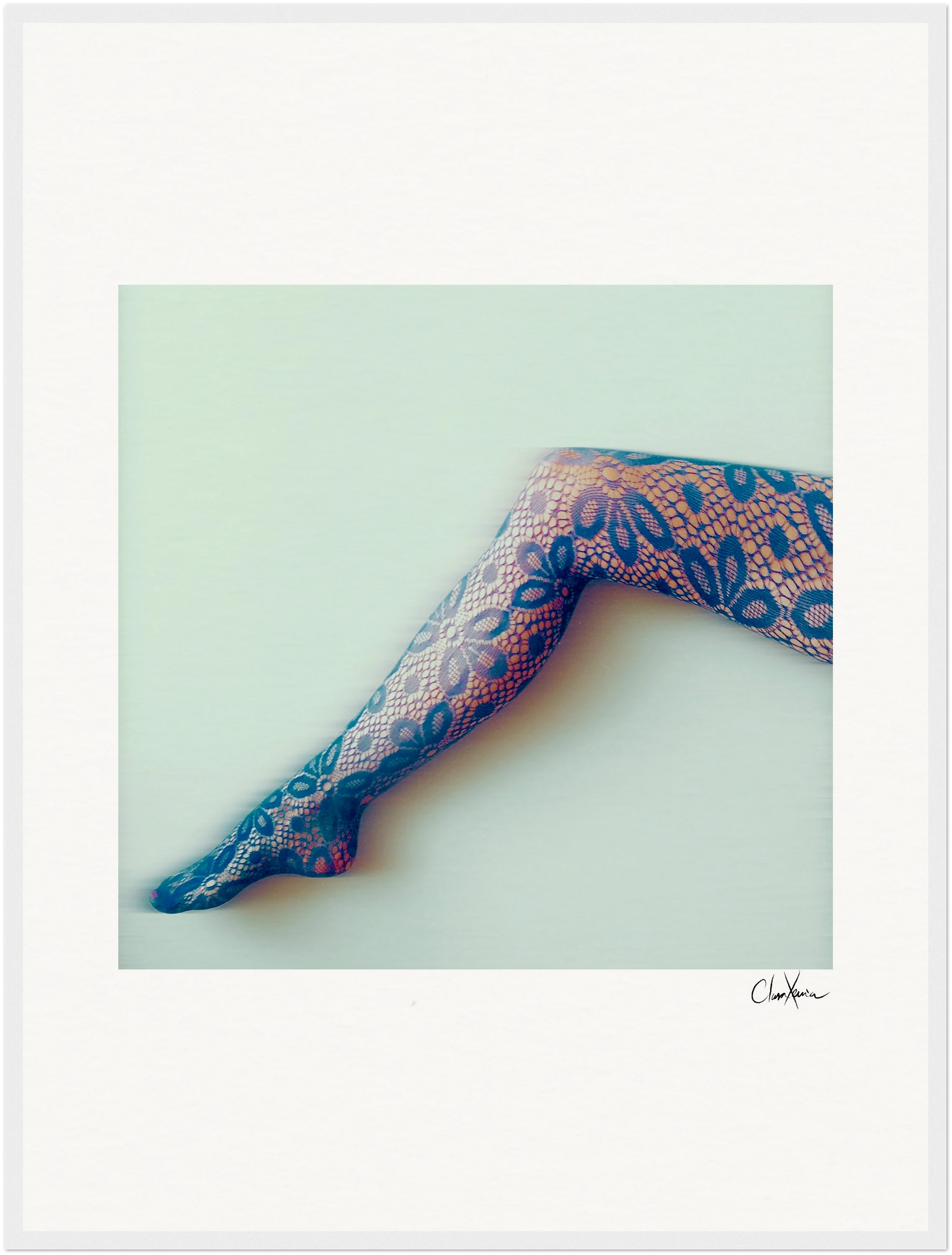 A single leg extended sideways, wearing patterned, lace-like stockings with a floral design, is set against a plain, light background—perfect as a fine art print to elevate any conscious interior design.