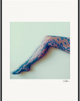 A single leg extended diagonally across a pale background, wearing patterned lace tights with a floral design. This fine art print is framed and signed in the lower right corner, making it ideal for mindful home decor.