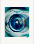 A close-up image of an Electrolux washing machine door features blue and green light reflections with circular patterns on the glass. This fine art print offers a soft, artistic blur, making it ideal as inspirational wall art for a mindful home decor.
