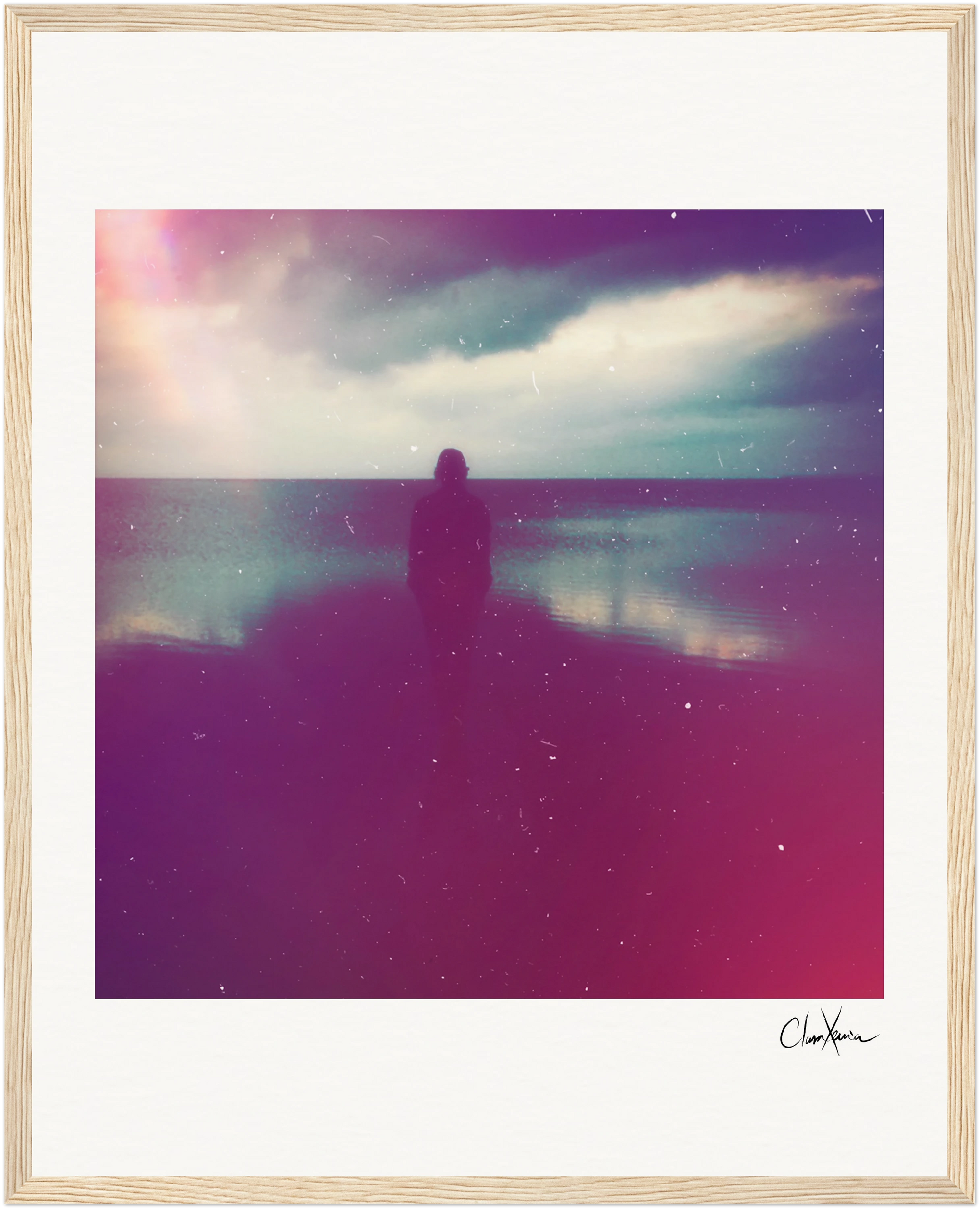 A silhouetted figure stands on a beach at sunset under a cloudy sky. The dreamy image, with pink and purple tones and a soft, grainy effect, is framed in light wood—perfect for mindful home decor.