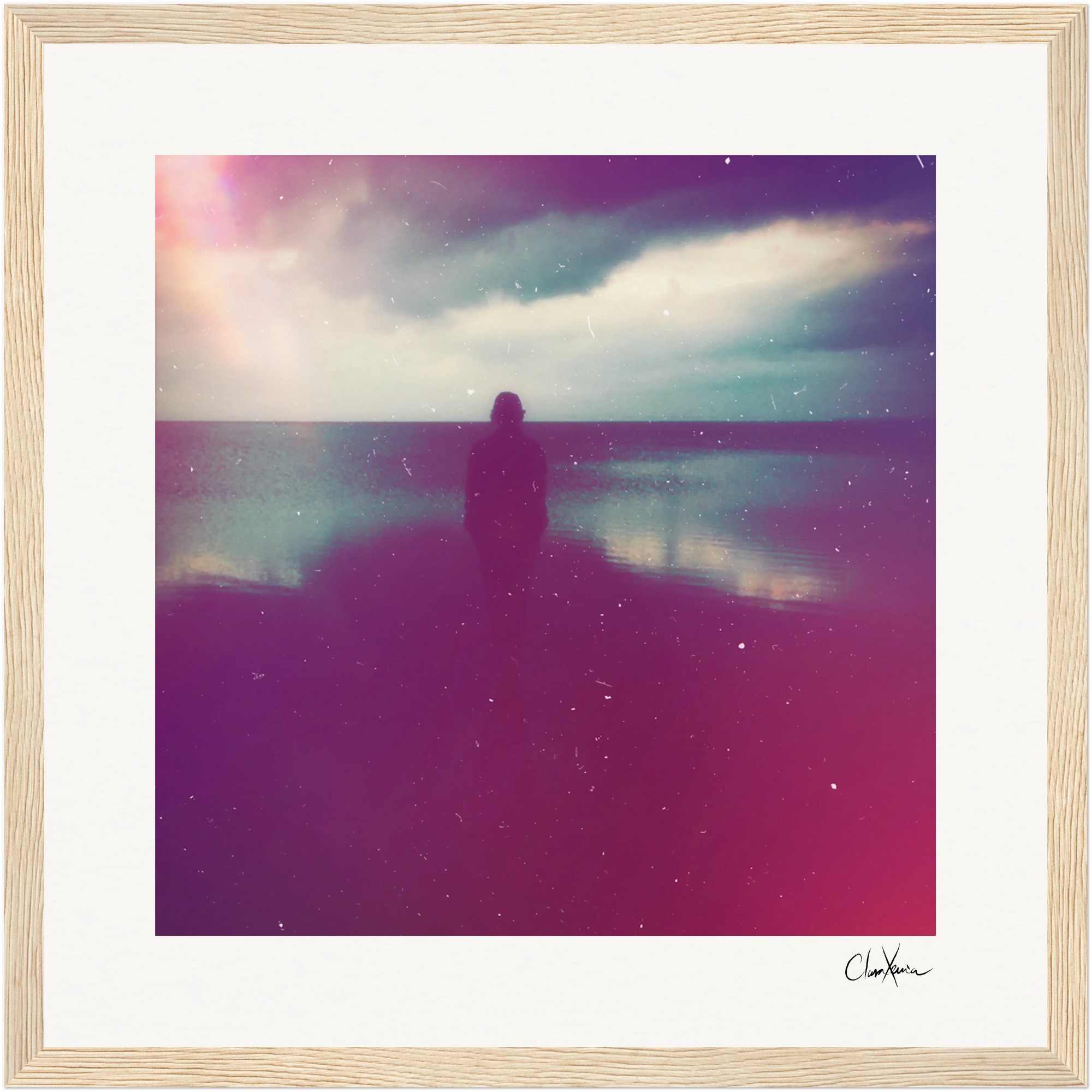 A person stands facing the ocean under a cloudy sky. The image, framed in a gallery-quality frame, features a soft, dreamy filter with pink and purple tones and light speckles—ideal as mindful home decor.