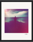 A silhouetted person stands by the water under a cloudy sky, enhanced with a dreamy filter in purple, pink, and blue. This fine art print features a white border, black frame, and a signature in the bottom right corner. Perfect for mindful home decor.