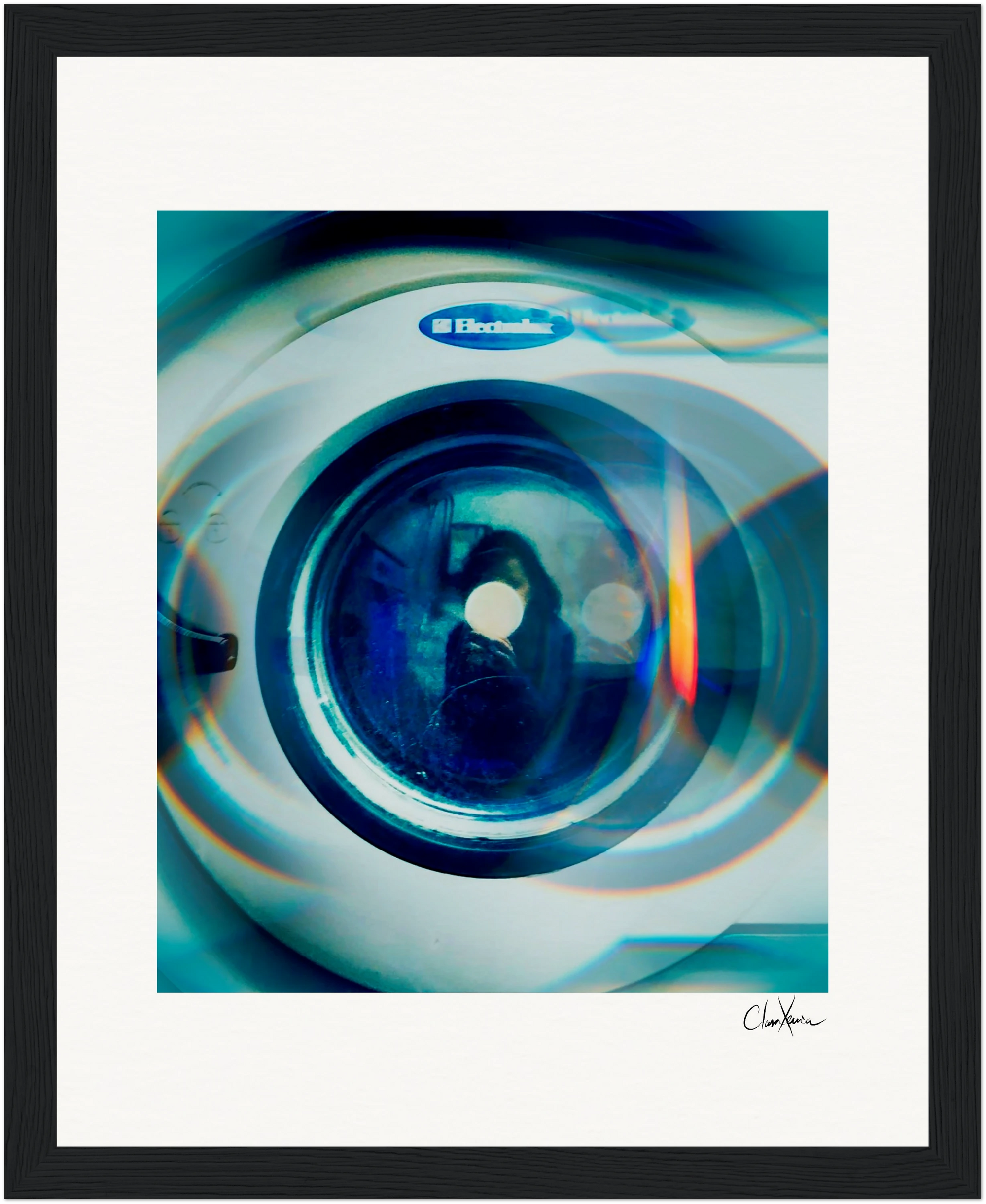 A close-up photo of an Electrolux washing machine door with blue-toned light reflections and circular lens effects, presented as inspirational wall art in a gallery-quality frame with a white mat and artist’s signature at the bottom right.