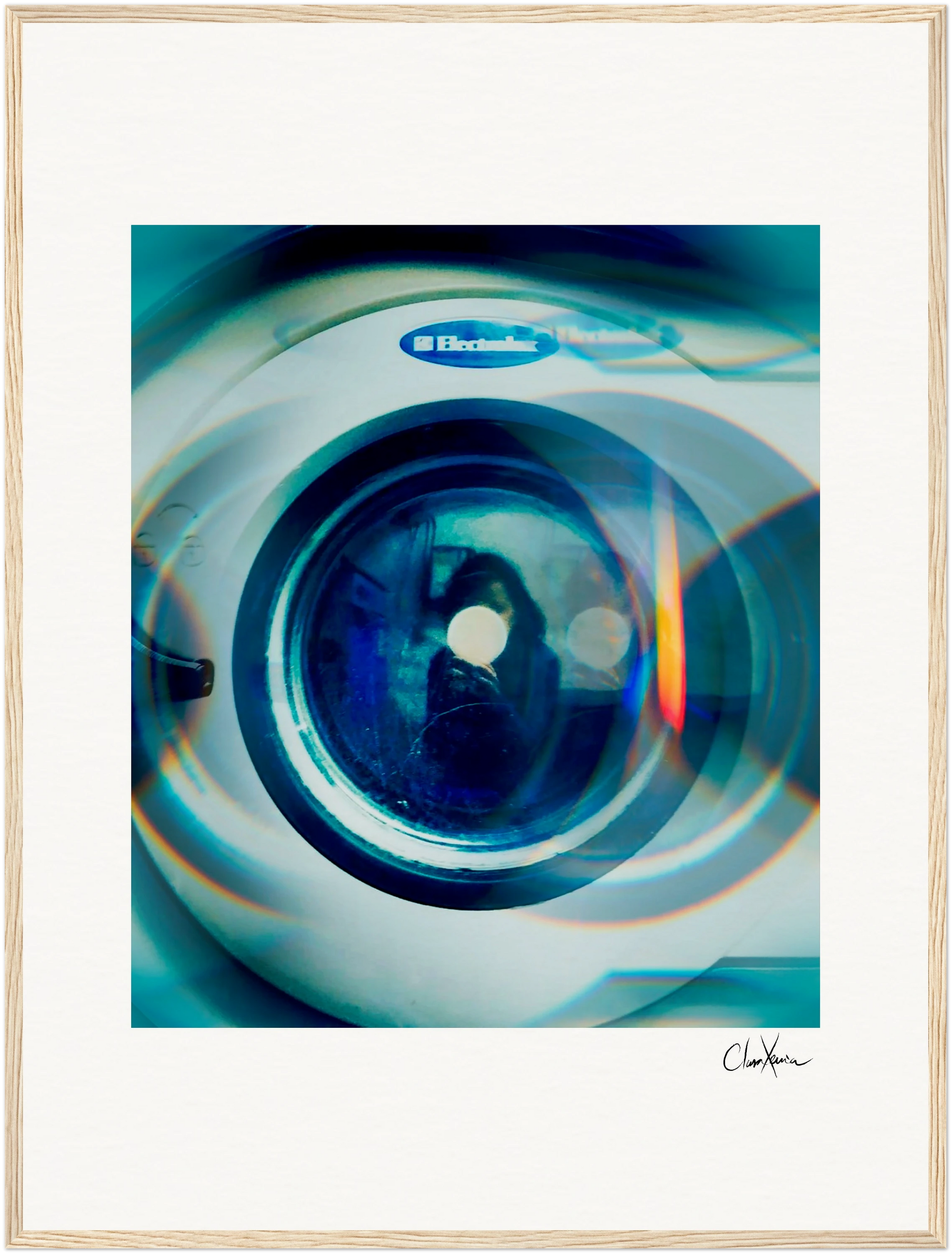 A close-up photo of an Electrolux front-loading washing machine door with blue and orange light reflections, presented as a fine art print. The image features a soft blur, a white border, and a gallery-quality frame of light wood.