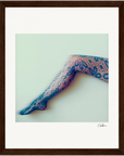 A single outstretched leg wearing blue floral lace patterned tights, set against a pale background. This framed wall art features a dark brown border and a signature in the bottom right corner—perfect for mindful home decor.