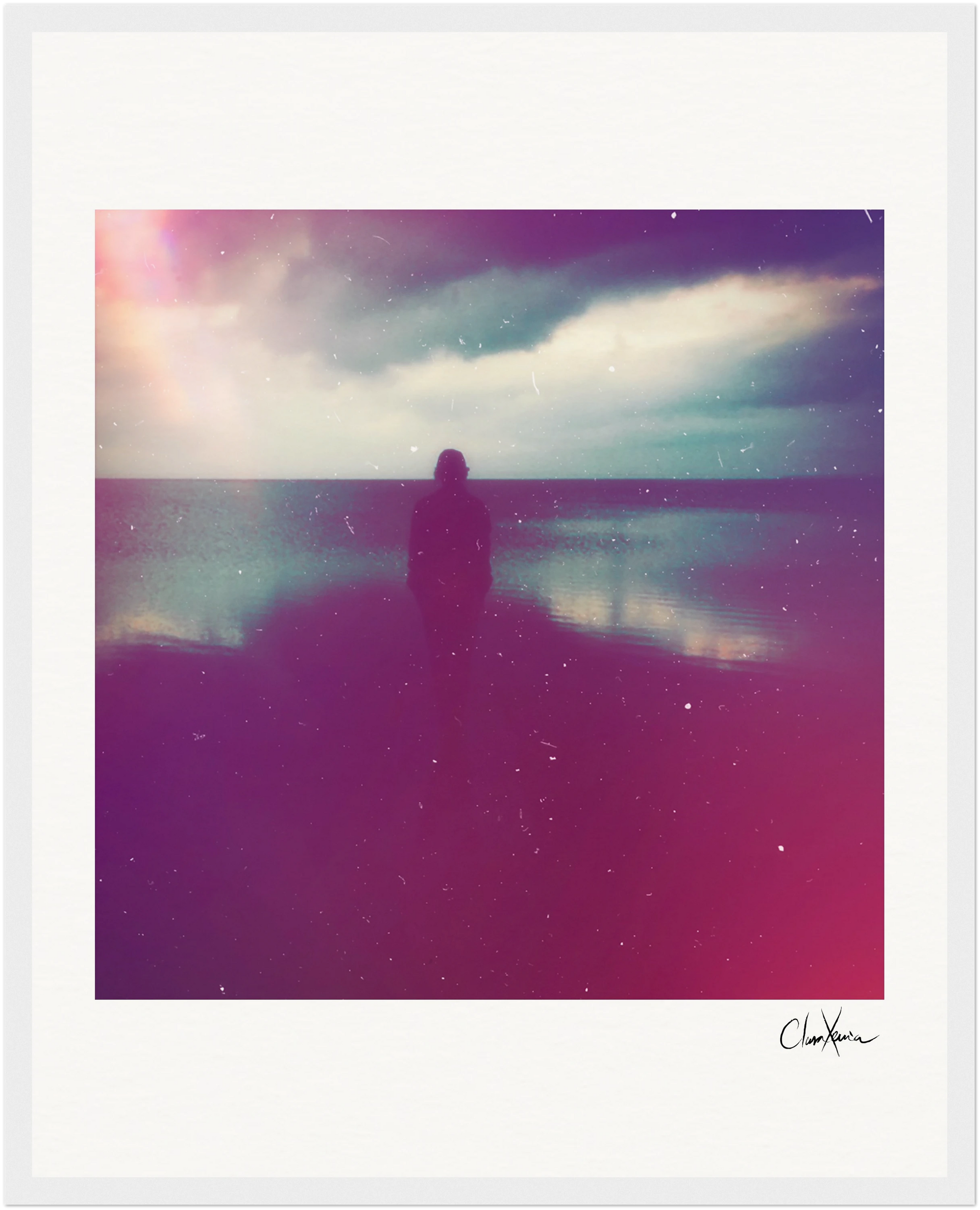 A silhouetted figure stands on a beach under a cloudy sky, with light flares and grainy effects creating a soft, dreamy look. This inspirational wall art features a white border and a signature in the corner—perfect for any gallery-quality frame.