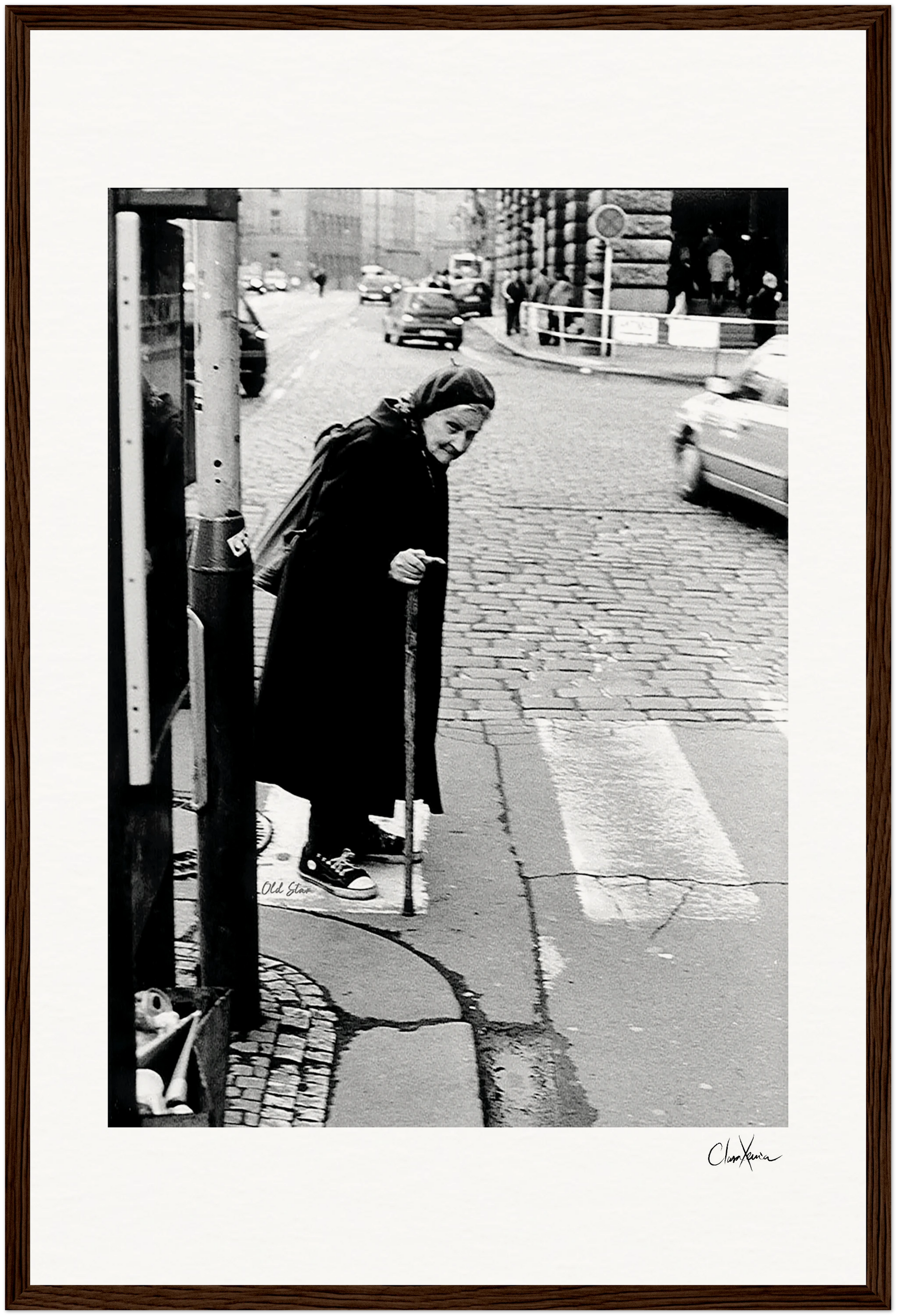 An elderly woman in a headscarf and dark clothing walks with a cane across a cobblestone street at a crosswalk, observed by cars and buildings—an evocative scene perfect for inspirational wall art or framed wall art in a mindful home decor setting.