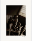 A man sits barefoot on a wooden chair, his arms resting on his knees, gazing thoughtfully into the distance. In black and white with soft focus and contrasted lighting, this fine art print is perfect as framed wall art for any conscious interior design.