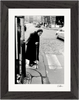 Black and white fine art print of an older woman with a cane at a crosswalk on a cobblestone street, cars and buildings behind her. Presented as inspirational wall art in a dark wooden frame.