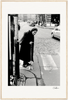 An elderly woman in a headscarf crosses a cobblestone street with her cane at a crosswalk. Cars and buildings line the background. This black and white fine art print adds timeless character to mindful home decor or inspirational wall art displays.