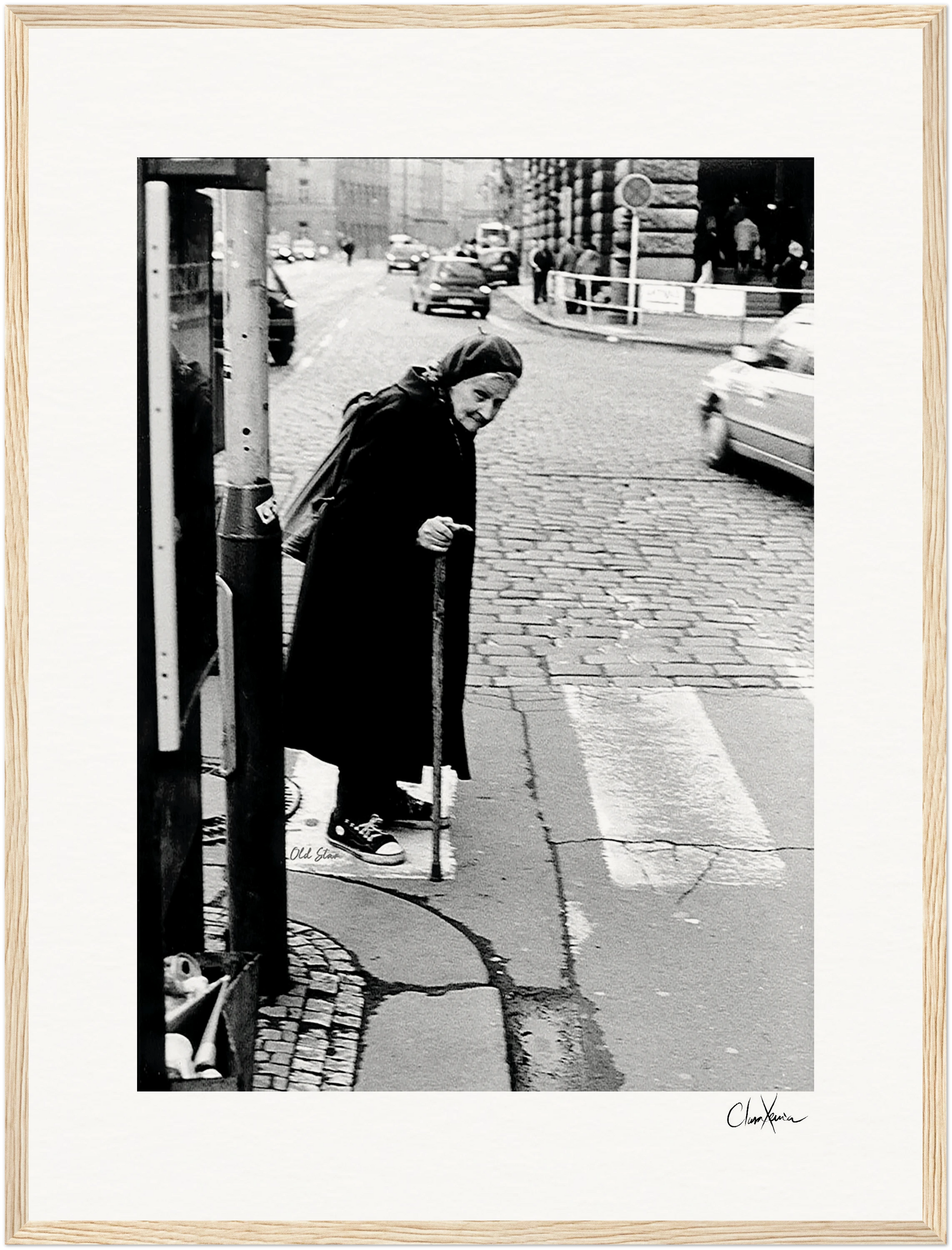 An elderly woman in a headscarf and coat uses a cane to cross a cobblestone street, with cars and pedestrians nearby. This scene captures timeless resilience, perfect as an inspirational wall art or fine art print in a gallery-quality frame.