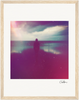 A silhouette stands at the edge of calm water under a cloudy sky. With a grainy, purple and pink overlay and light wood frame, this fine art print is inspirational wall art, complete with an artist’s signature in the lower right corner.