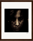 A dark, grainy close-up portrait of a person with long hair partially obscuring their face, set against a white mat and brown wooden frame. This fine art print features a serious expression, making for inspirational wall art in any space.