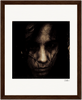 A dark, grainy close-up portrait of a person with long hair partially obscuring their face, set against a white mat and brown wooden frame. This fine art print features a serious expression, making for inspirational wall art in any space.