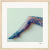 A single extended leg wearing patterned, lace-like stockings is photographed against a pale, neutral background. This fine art print features a soft, artistic effect and is framed with a light wood border for mindful home decor.