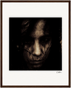 A dark, grainy close-up image of a person’s face with an intense expression, partially obscured by shadows and hair. This inspirational wall art is centered within a gallery-quality frame and white mat. A signature appears in the lower right corner.